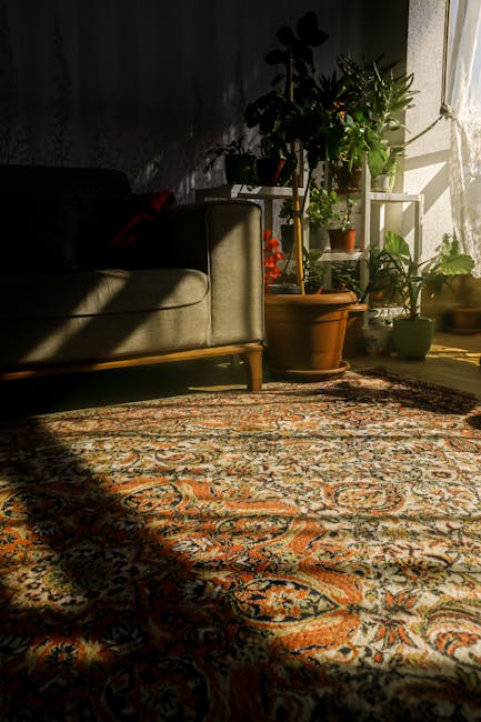 A residential living room corner featuring a traditional patterned area rug with intricate designs in warm tones, fresh sunlight brightly illuminating the space, and several potted houseplants on a wh